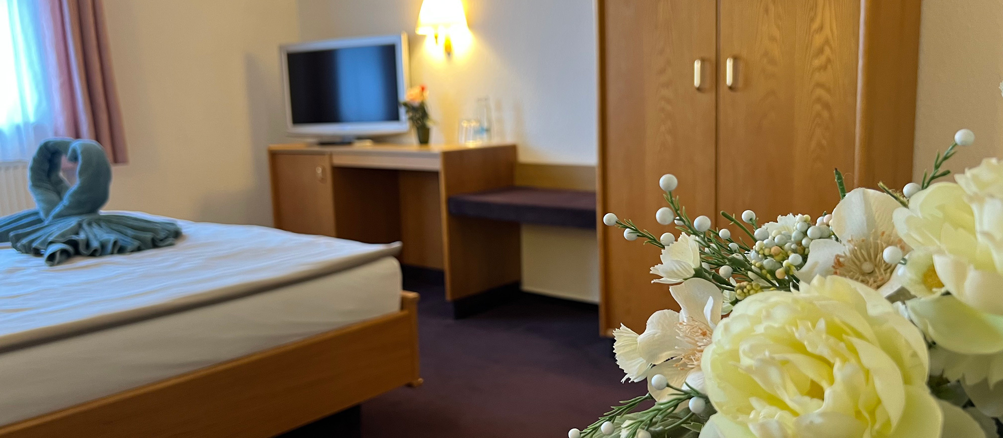 Hotelzimmer mit Bett, Schrank und Blumen